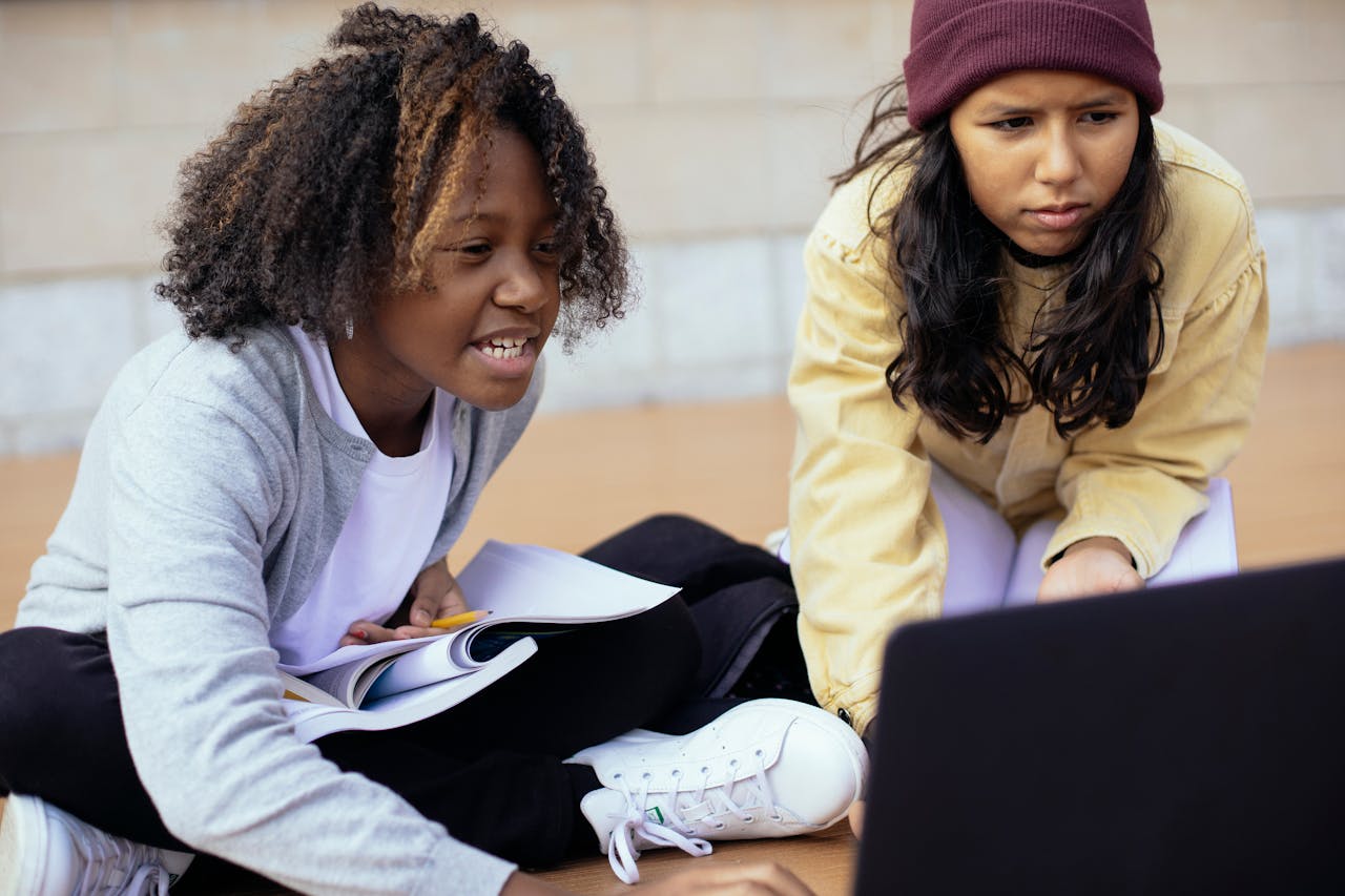 Crop attentive diverse schoolchildren watching laptop while studying on street
